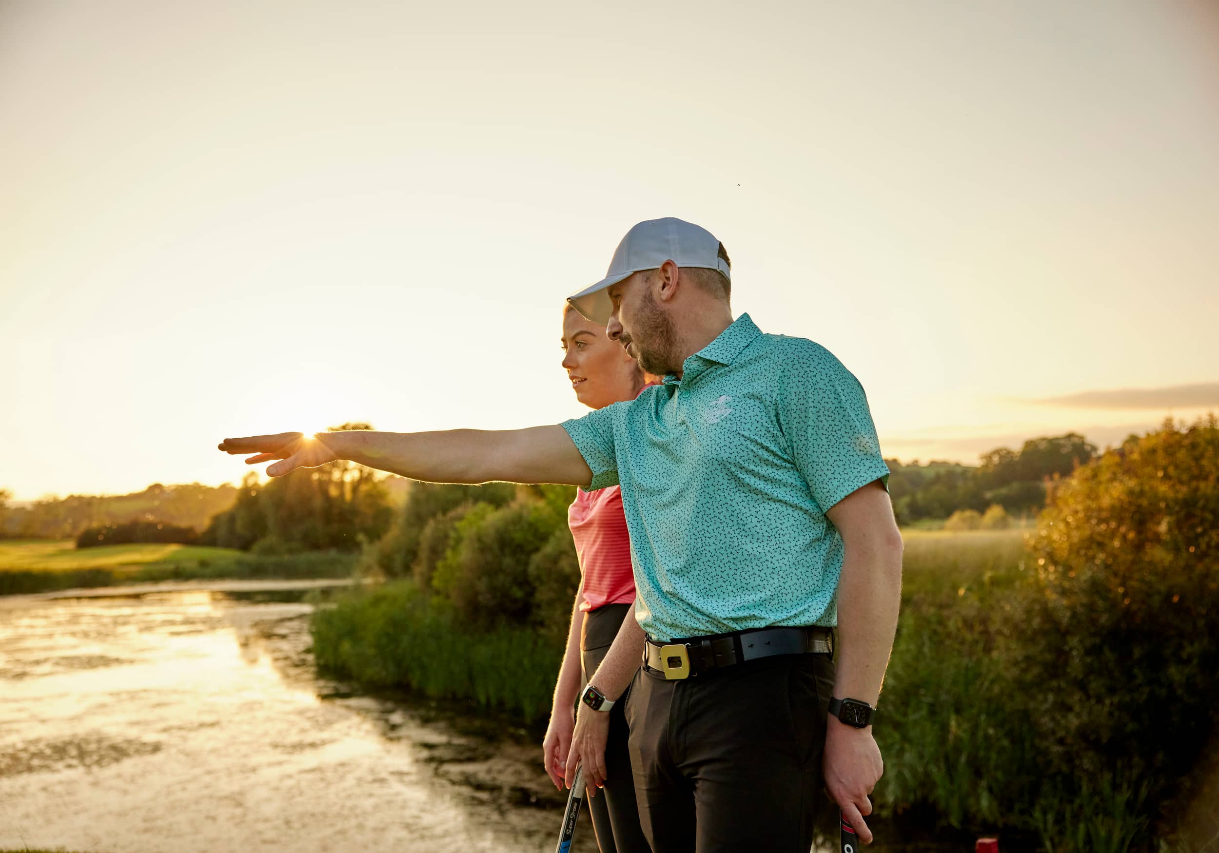 Two golfers standing in a bunker at Celtic Manor, pointing toward the green.